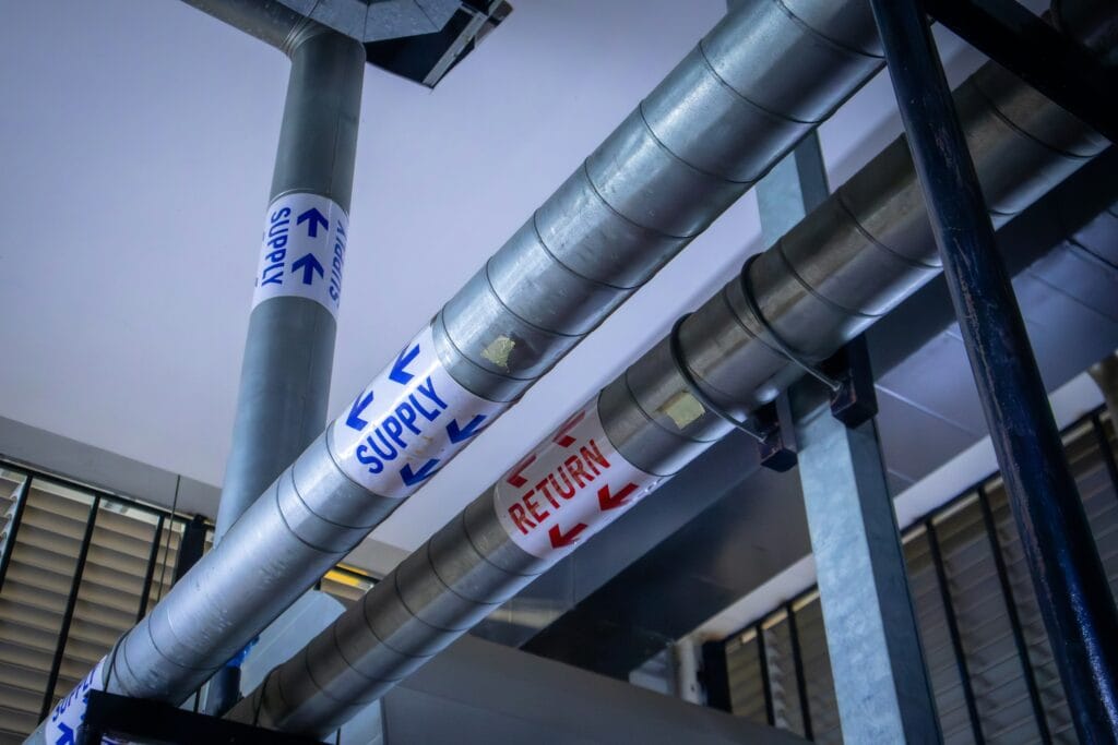 Large metal air ducts labeled "SUPPLY" and "RETURN" with blue and red arrows are part of an HVAC system installed on a building ceiling in TX, often seen in facilities needing reliable airflow such as carpet cleaning Houston County businesses.