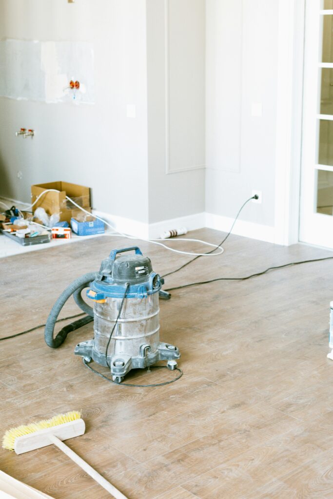 A vacuum cleaner, broom, and carpet cleaning Houston County supplies are scattered on the floor of a TX room under renovation, with unfinished walls and tools in the background.